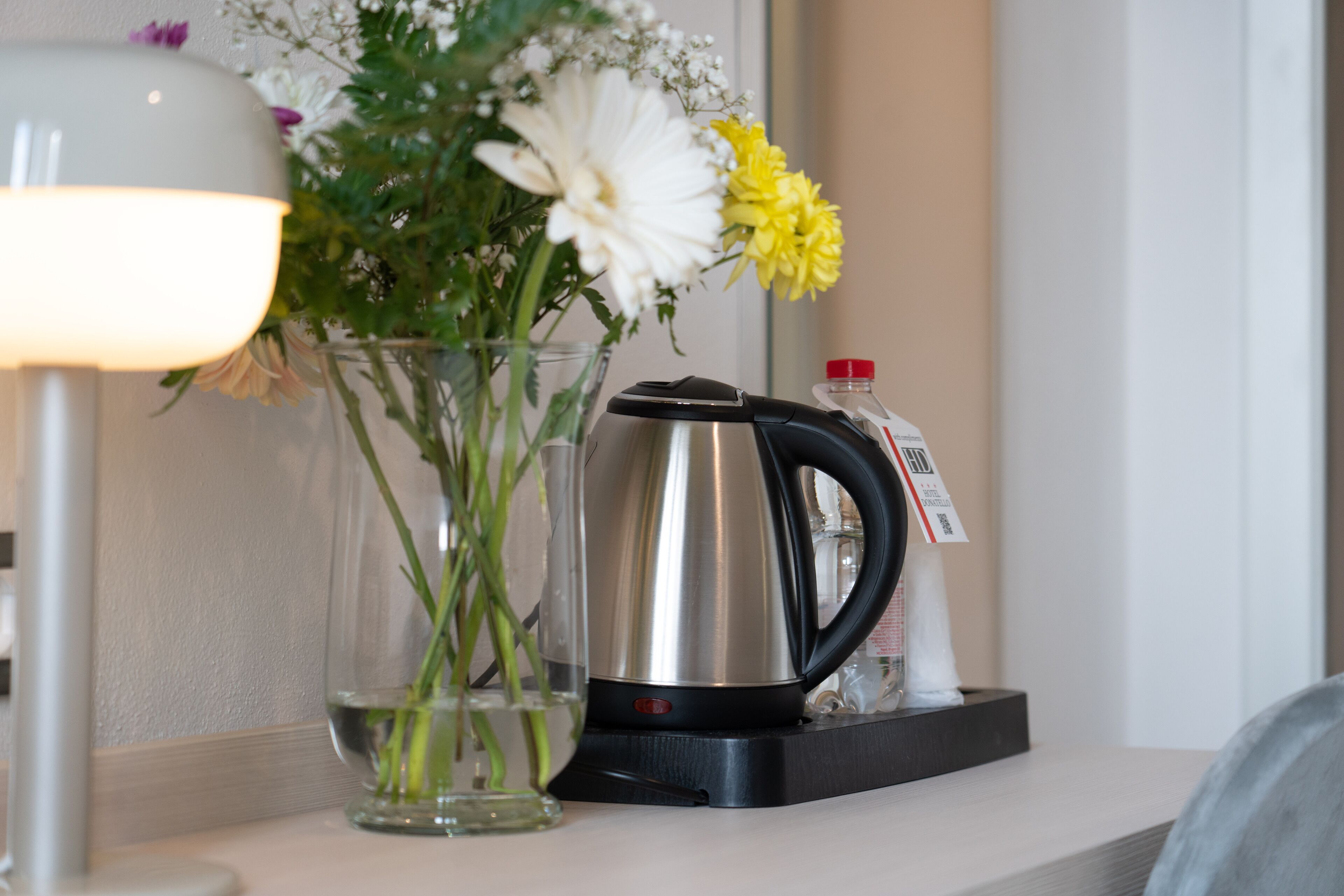 A clear glass vase with flowers and a stainless steel kettle on a countertop.