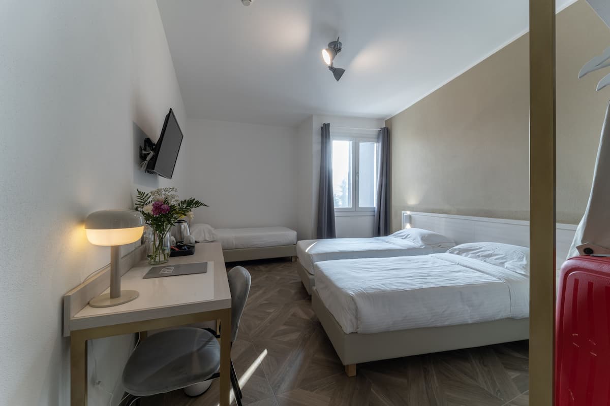 A hotel room with a desk, two beds, a TV, and a window with curtains.