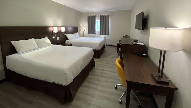 Een hotelkamer met twee bedden, een bureau, een stoel, een televisie en een raam met gordijnen.
