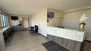 Een hotel receptie met een marmeren balie, twee blauwe stoelen, een kleine potorkidee en een flatscreen televisie aan de muur.