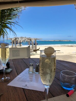 Ein Tisch mit einer Speisekarte, zwei Sektgläsern und einem Blick auf einen tropischen Strand im Hintergrund.