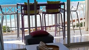 Un balcó amb vista a l'oceà, dues cadires, una taula petita i un coixí vermell.