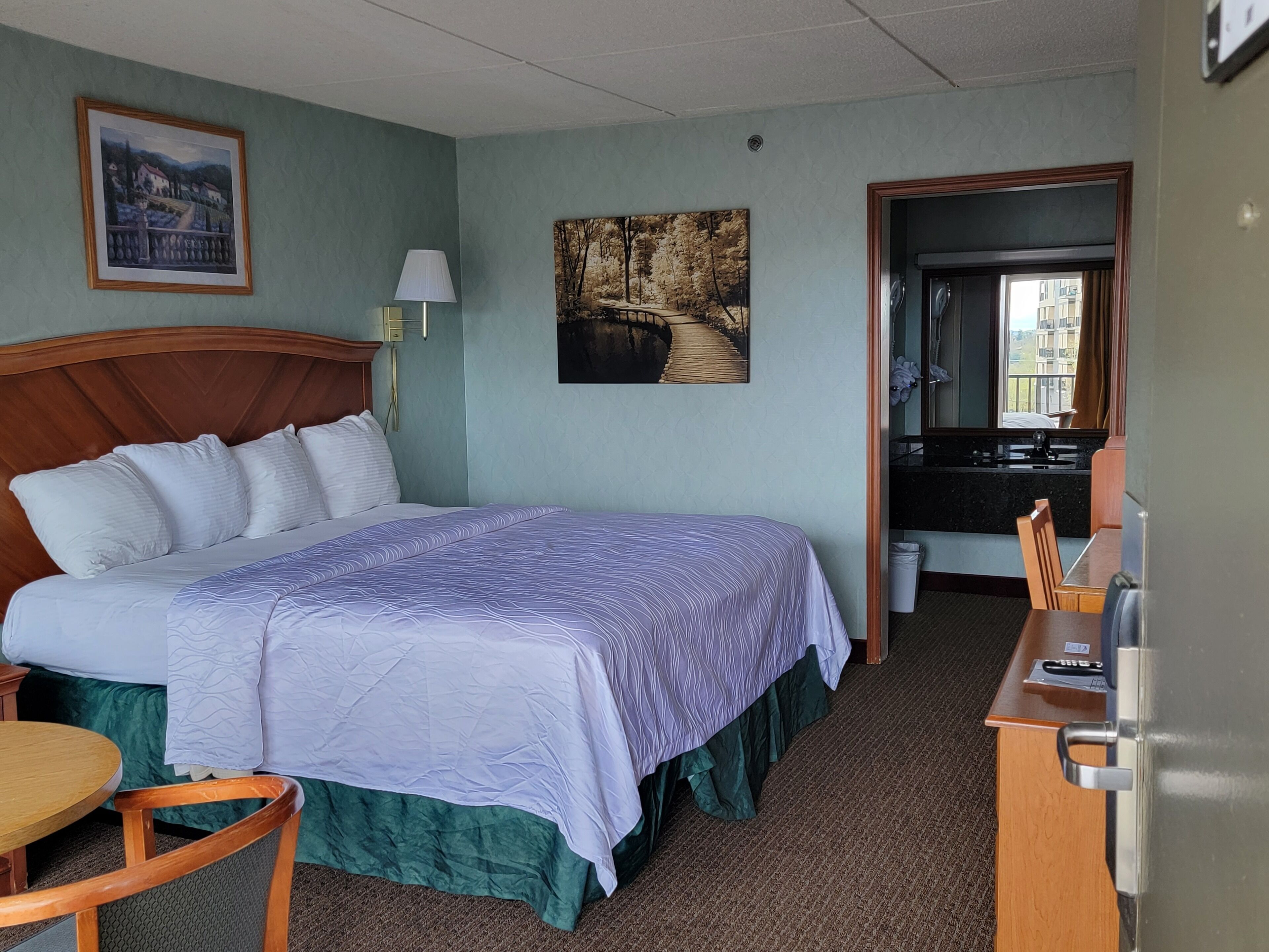 Een hotelkamer met een groot bed, een bureau, een stoel, een lamp en twee schilderijen aan de muur.