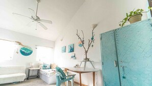 Un salon lumineux avec un canapé blanc, un fauteuil bleu, une table en bois et un ventilateur de plafond.