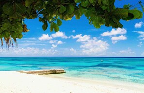 A beach with clear turquoise waters, white sand, and a distant boat.