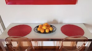 Een eettafel met twee stoelen, een schaal oranjes en twee rode placemats.
