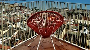 Een rode stoel op een balkon met uitzicht over een stadsgezicht en een heldere blauwe lucht.