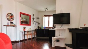 Een woonkamer met houten vloer, een rode fauteuil, een aan de muur bevestigde televisie en een open haard.