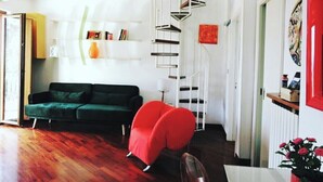 Een moderne woonkamer met een spiltrap, een groene bank, een rode fauteuil en een eettafel.