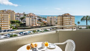 A balcony with a table set for breakfast, overlooking a coastal town with buildings and a beach. - ALFRESCO STAYS  BenalBeach Sea & Sun (Benalmádena)