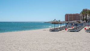 A beach with sun loungers and umbrellas, a hotel in the background, and a clear blue sky. - ALFRESCO STAYS  BenalBeach Sea & Sun (Benalmádena)