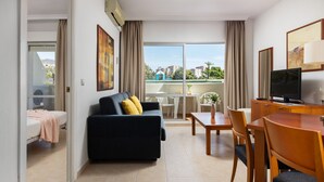 Moderni hotellihuone, jossa on sohva, ruokapöytä, tuolit ja televisio.