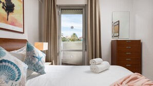 Hotellihuone, jossa on sänky, lipasto, peili ja ovi, joka johtaa parvekkeelle.