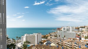 Un paysage urbain côtier avec vue sur la mer, comprenant un mélange de bâtiments résidentiels et d’hôtels, dont certains sont dotés de balcons et de panneaux solaires.
