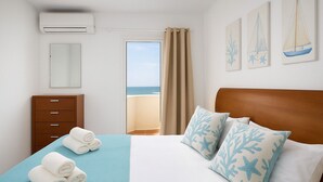 Une chambre d’hôtel avec un lit, une commode en bois, une fenêtre donnant sur la mer et un mur décoré d’œuvres d’art sur le thème de la marine.