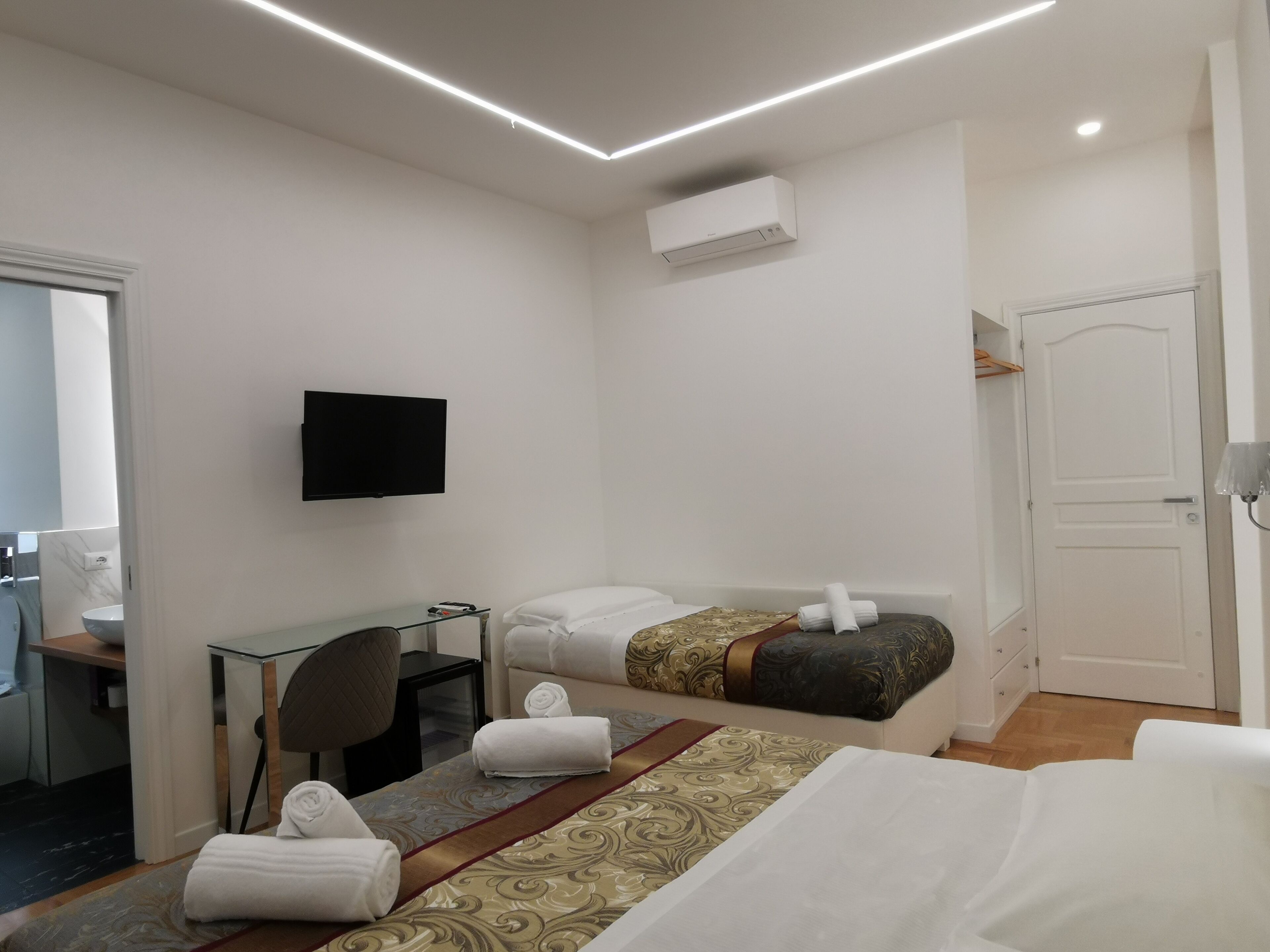 A hotel room with a bed, a desk, a chair, a television, and an air conditioning unit.