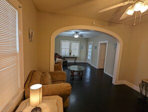 A spacious living room with a dark floor, a round glass coffee table, and a sofa. - 3 bed Close to Pleasure Pier! Minutes to the Strand! (Galveston)