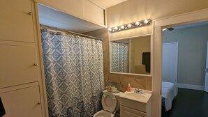 Un bagno con tenda da doccia decorata, un water, un lavandino con specchio sopra e una porta che dà su un'altra stanza.
