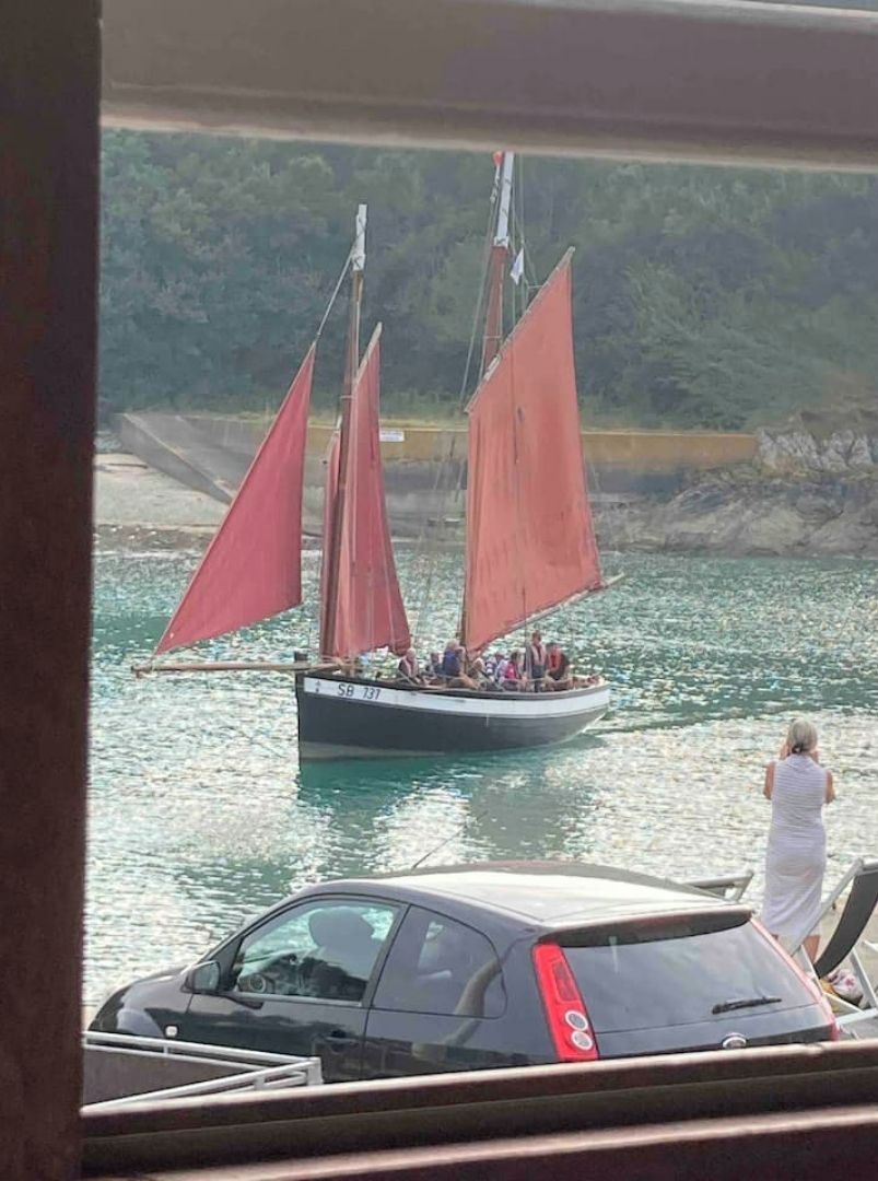 A boat with red sails docked near a rocky shoreline.
