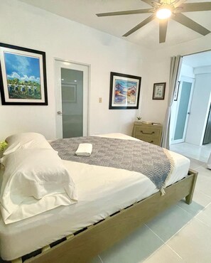 Une chambre à coucher avec un lit, un ventilateur de plafond et des œuvres d’art encadrées accrochées aux murs.