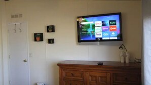 A living room with a flat-screen TV mounted on the wall displaying various streaming services. There is a wooden cabinet below the TV and a door to the left.