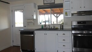 A kitchen with white cabinets, a stainless steel dishwasher, an oven, and a window with a view of the outdoors.