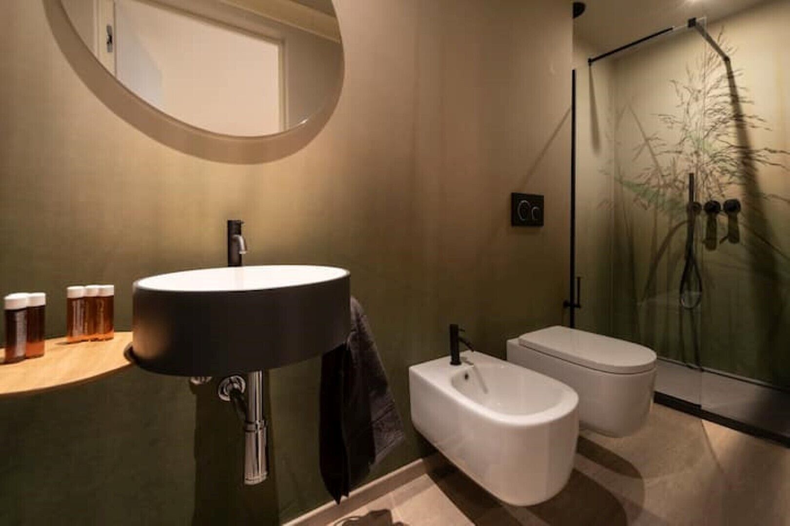 Ein modernes Badezimmer mit rundem Spiegel, großem Waschbecken, Toilette und einer Duschkabine aus Glas.