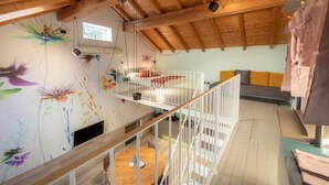 A loft-style room with a wooden ceiling, a bunk bed, a colorful mural, and a window.