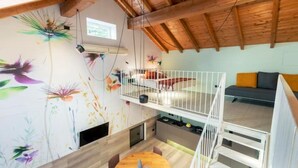 A loft-style room with a wooden ceiling, a bunk bed, a dining area with a round table, and a colorful wall mural.