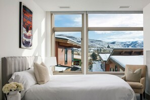 Panoramic mountain views from the large window, a comfortable bed, and a cozy chair invite relaxation.