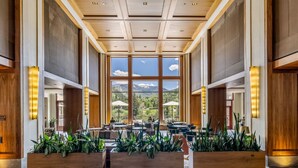 Un espace intérieur vaste et lumineux, doté de grandes fenêtres offrant une vue sur les montagnes, de lambris en bois et de plantes d’intérieur.