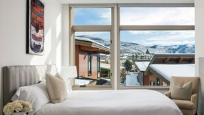A hotel room with a large window offering a view of a snowy mountain landscape and a town below. - Pop Art Villa Riverfront | King Room (Avon)