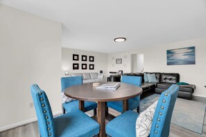 Una sala de estar moderna con una mesa redonda, sillas tapizadas en azul, un sofá gris y un sofá de cuero negro.