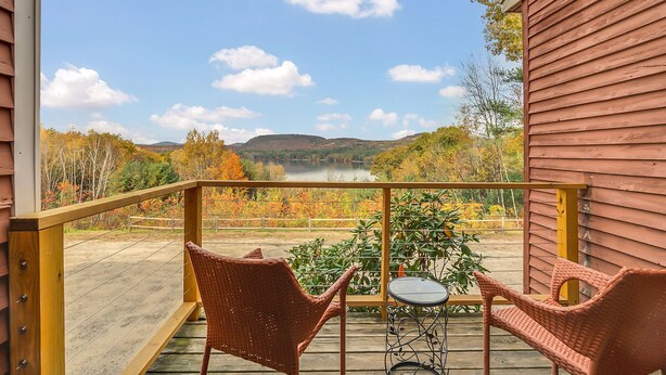 Een houten terras met rieten stoelen en een kleine tafel, met uitzicht op een meer en herfstkleuren.