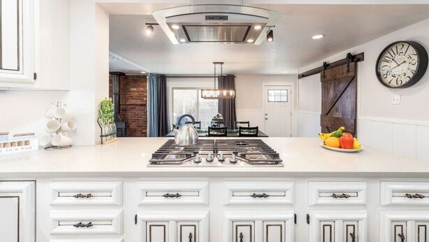 Une cuisine moderne avec un îlot central, des meubles blancs et une grande horloge au mur.