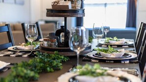 Une table à manger dressée avec des assiettes, des couverts et des verres, agrémentée d’un centre de table décoratif et de quelques éléments de verdure.