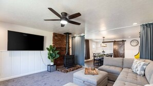 Un salon moderne doté d’un téléviseur à écran plat, d’une cheminée, d’un ventilateur de plafond et d’un coin repas avec une table et des chaises.