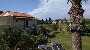 Una casa con techo de tejas rojas, un balcón y paneles solares en el jardín.