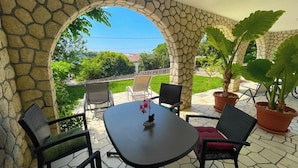 A patio with a stone archway, a round table, and four chairs. - Holiday apartment with terrace and air conditioning (Novi Vinodolski)