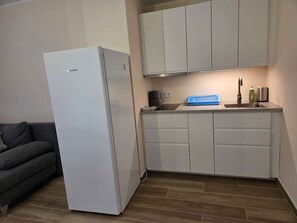 Eine kompakte Küche mit weißen Schränken, einer eingebauten Spüle und einem grauen Sofa im angrenzenden Wohnbereich.