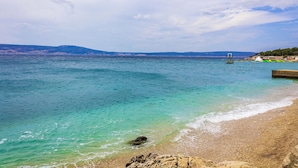 A coastal beach with clear turquoise waters, a rocky shoreline, and distant hills. - Holiday apartment with terrace and air conditioning (Novi Vinodolski)