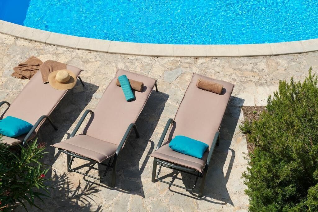 A poolside area with three sun loungers, each with a cushion and a towel.