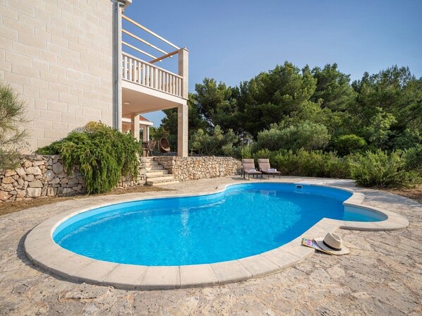 A swimming pool with a stone deck, a stone wall, and a covered outdoor seating area with chairs. - Villa Sonia with private pool, 4 bedrooms and beautiful garden (Stari Grad)