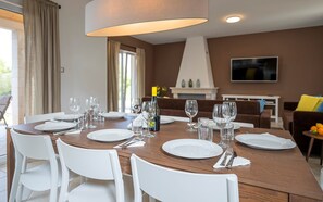 Un comedor con una mesa de madera dispuesta para seis personas, sillas blancas y una lámpara moderna.