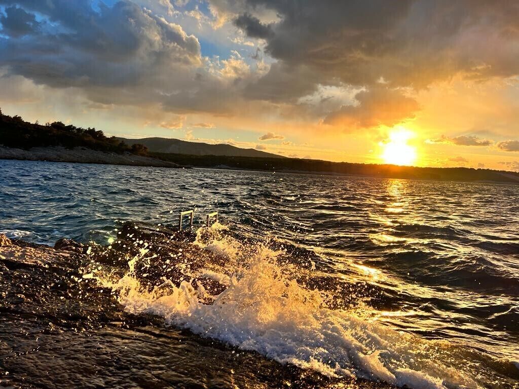 Un atardecer sobre una masa de agua con olas rompiendo en una costa rocosa.
