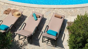 Ein Poolbereich mit drei Liegestühlen, jeweils ausgestattet mit einem Handtuch und einem Hut.
