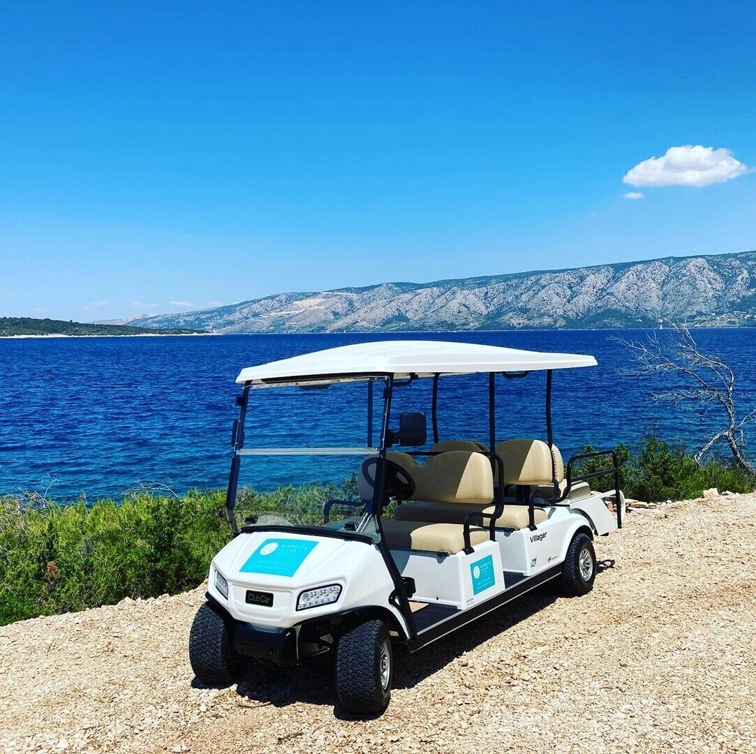 Een golftrolley geparkeerd op een grindpad, met een mooi uitzicht op een wateroppervlak en bergen op de achtergrond.
