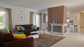 Un salon moderne avec un canapé marron, une table basse blanche et une cheminée. On aperçoit à l’arrière-plan un coin repas avec une table et des chaises.