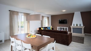 A modern living room with a brown sofa, a wooden dining table with chairs, a TV mounted on the wall, and a fireplace. - Holiday villa Stella with private pool and 3 bedrooms (Stari Grad)