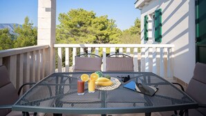 En balkon med et bord dækket til to personer, med et metalbord, to stole, en pude, en flaske og en skål med frugt.